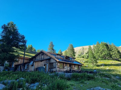 Vue du refuge, situé sur une butte au milieu de la végétation environnant. Espace de terrasse devant l'entrée principale, [...]