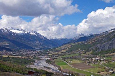 Barcelonnette et Faucon de Barcelonnette en début de printemps, les sommets sont encore bien enneigés, nuages de beau temps.